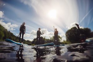 Small group of teenagers enjoying paddleboarding together. One is doing a handstand, the rest are talking and laughing.